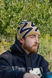 Slug Beanie - Mustard by Quasi Skateboards on a person outdoors, featuring a bold black pattern on mustard knit. Black hoodie.