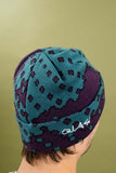 Quasi Skateboards Dither Beanie in Eggplant, featuring a teal blue and purple dotted pattern, worn on a person's head.